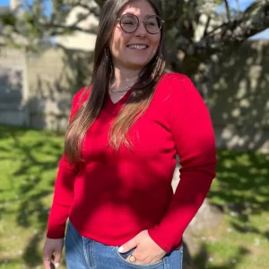 Pull col V en 100% laine mérinos extrafin rouge sombre porté avec un jean par une femme dans un jardin ensoleillé