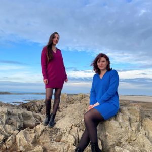 Robes en mérinos extrafin portées par deux femmes. La première, sur la gauche, debout sur un rocher portant la robe en couleur prune. Et une deuxième, sur la droite, assise sur un rocher portant la robe de couleur cobalto.
