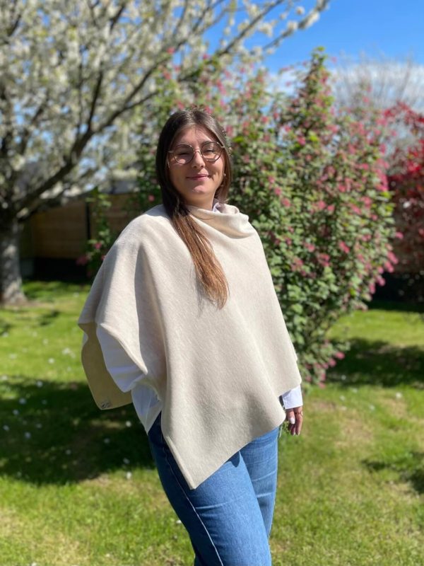 Poncho en 100% mérinos extrafin couleur beige porté par une femme dans un jardin ensoleillé