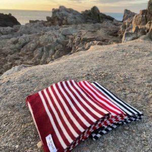 trois écharpes rayées pliées et posées sur un rocher avec la mer au fond pendant un coucher de soleil