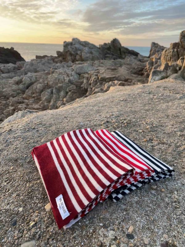 trois écharpes rayées pliées et posées sur un rocher avec la mer au fond pendant un coucher de soleil